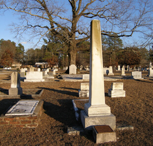 Ellen Schattschneider, Bishop Andrew memorial obelisk in the Andrew family plot (foreground) and the Kitty Tablet at the base of the Gateway Oak (background), Oxford, Georgia, 2005. Ellen Schattschneider, Bishop Andrew memorial obelisk in the Andrew family plot (foreground) and the Kitty Tablet at the base of the Gateway Oak (background), Oxford, Georgia, 2005.