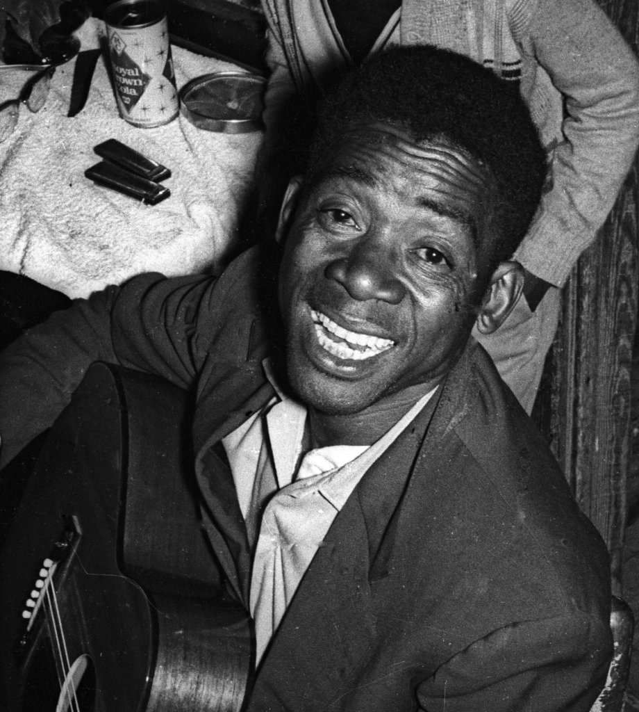 Bud White holding a guitar, smiling or singing, looking up at the camera.