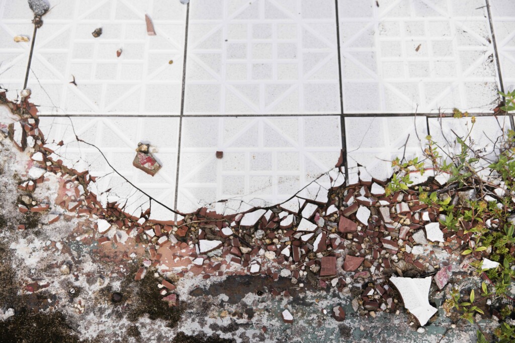 Broken sidewalk tile, an apt metaphor for what Waisman has catalogued: the bombardment of a community that will end in permanent exile.